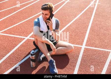 Sorridente sportivo finito l'esecuzione presso lo stadio, riposo, parlando al telefono cellulare Foto Stock