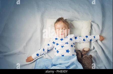 Sei anni bambino che dorme nel letto con la sveglia Foto Stock