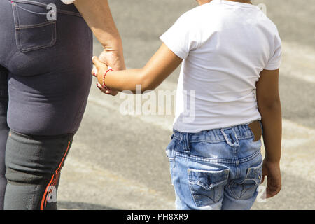 Madre attraversando la strada tenendo la mano dei suoi figli Foto Stock