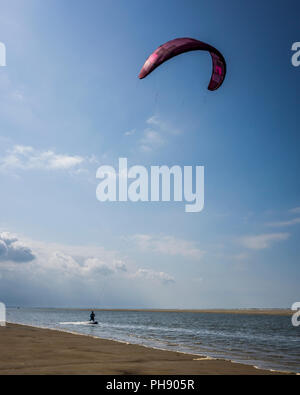 Am Strand Langeoog. Germania Deutschland. Una persona è kitesurf lungo il bordo dell'acqua della spiaggia di sabbia. Una stretta striscia di acqua di mare si estende lungo la spiaggia è ideale per gli sport acquatici. Fotografato su una luminosa giornata di sole principalmente con il cielo limpido ad eccezione di poche nuvole di luce. Foto Stock