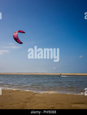 Am Strand Langeoog. Germania Deutschland. Una persona è kitesurf lungo il bordo dell'acqua della spiaggia di sabbia. Una stretta striscia di acqua di mare si estende lungo la spiaggia è ideale per gli sport acquatici. Fotografato su una luminosa giornata di sole principalmente con il cielo limpido ad eccezione di poche nuvole di luce. Foto Stock