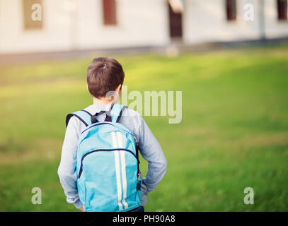 Ragazzo con zaino in spalla davanti a un edificio scolastico Foto Stock