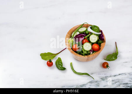 Insalata fresca in ciotola di legno su marmo bianco pietra Foto Stock