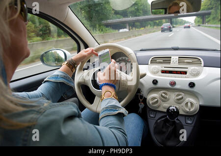 BOTTROP, Germania - 16 agosto 2018: una donna bionda sta leggendo il suo whatsApp sullo smartphone mentre si guida su una strada in piena velocità. Foto Stock