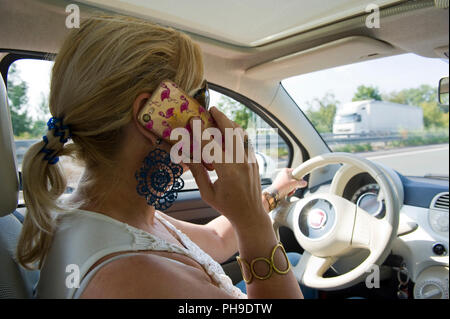 BOTTROP, Germania - 16 agosto 2018: una donna bionda sta chiamando con il suo smartphone mentre si guida su una strada in piena velocità. Foto Stock