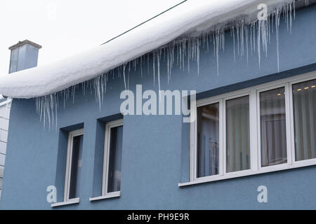 Grandi ghiaccioli e neve sospesi dal tetto - primo piano Foto Stock