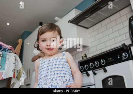 Bassa nagle vista di una bambina guardando la telecamera. Ella si fermò in cucina e tirando uno sfrontato espressione facciale con la sua linguetta sporgente Foto Stock