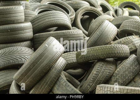 Una foto di molti vecchi pneumatici usati a sinistra su una discarica di rifiuti. La foto di un problema ecologico e di emergenza. Foto Stock