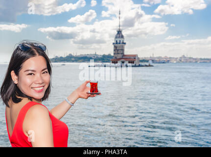 Bella donna cinese detiene il tradizionale tè turco con Maiden's Tower vista su sfondo in Istanbul, Turchia Foto Stock