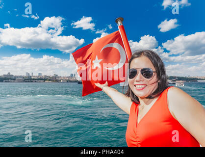 Bella donna cinese tocca bandiera turca mentre andando sul traghetto a Istanbul, Turchia Foto Stock