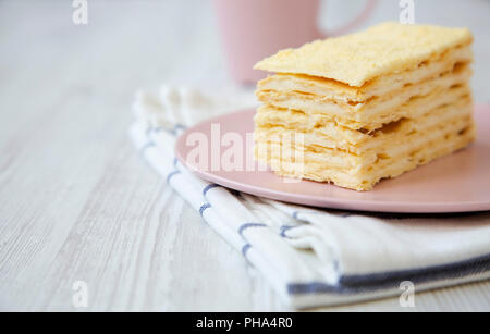 Pezzo di torta di Napoleone sulla piastra rosa su bianco tavolo in legno, close-up. Foto Stock