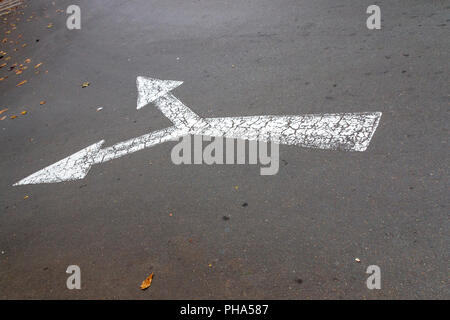 Una vista ravvicinata di un bianco di sdoppiamento di direzione cartello stradale freccia per il traffico in senso contrario Foto Stock