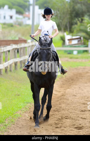 Bambina in sella a un cavallo nero Foto Stock