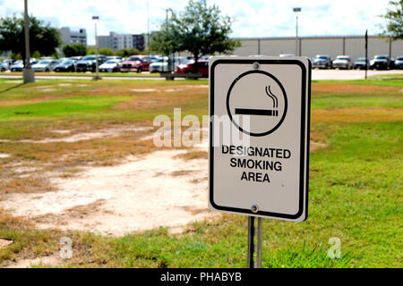 Area fumatori cartello fuori con parcheggio in background, bianco con stampa nera.. Foto Stock