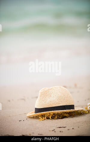 Bel cappello di paglia recante sulla sabbia. Bella spiaggia dell'oceano sullo sfondo. All'esterno. Tempo di vacanza. Fine delle vacanze estive. Sognando di vacanze al mare Foto Stock