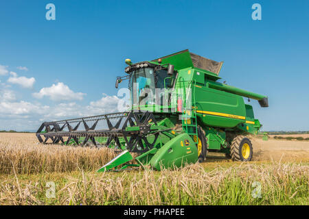 Un John Deere mietitrebbia Hillmaster harvester a lavorare su un raccolto di orzo primaverile contro un cielo blu sullo sfondo Foto Stock