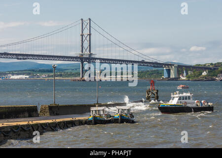 Queensferry, Scotland, Regno Unito - 14 Giugno 2012: Forth Road Bridge di sospensione su Firth of Forth tra il cielo blu e l'acqua. Pilota di Smit barche ormeggiate fino fr Foto Stock