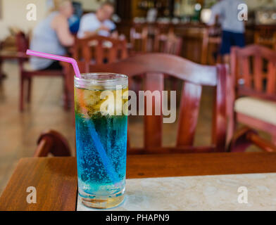 Frosty giallo e blu di bevanda alcolica, con la formazione di condensa sul vetro, servito in un resort cubano, sfondo con persone sfocata. Foto Stock