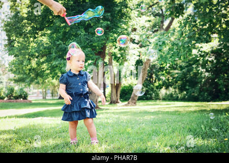 Ritratto di carino adorabili poco ragazza caucasica bambino in vestito blu in piedi nel prato di campo al di fuori del parco, rendendo le bolle di sapone, lifestyle infanzia Foto Stock