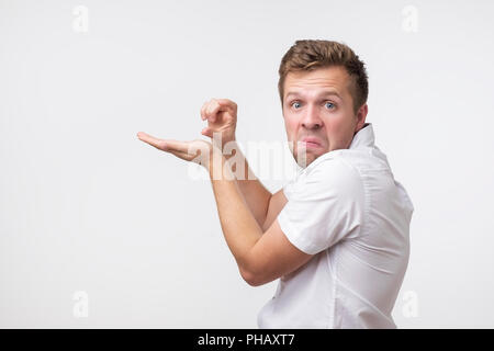 Positivo uomo bello mostra qualcosa di molto piccolo o piccola, essendo in dubbio l'umore, pone contro whitebackground. Foto Stock