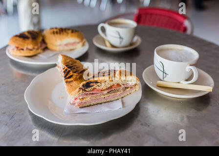 Autentico sandwich cubano alla griglia a strati con prosciutto e formaggio, pomodori e sottaceti. Accompagnata da una demitasse di caffè e latte vaporizzato e servita wi Foto Stock