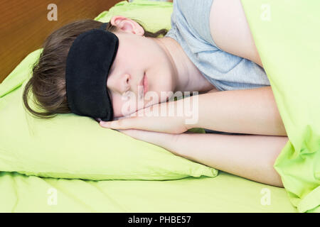 Ragazza adolescente in maschera nera dorme sul lino verde Foto Stock