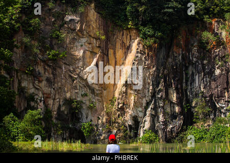 Vista posteriore di una donna in berretto rosso, si sta rilassando e connettendo con il mondo della natura in un parco delle cave di laghetti. Singapore. Foto Stock