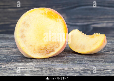 Tagliare pesca matura con tracce all'interno di rot e degrado, close-up di frutta sul bordo di taglio Foto Stock