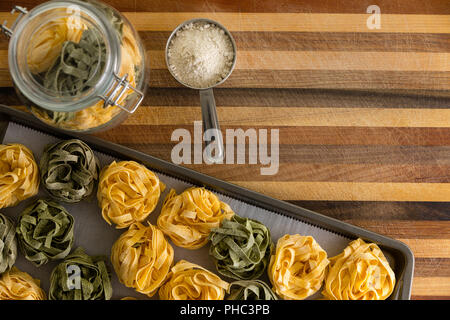 Preparata di fresco essiccato fettuccine con farina di grano duro ingrediente in un setaccio vista dall' alto verso il basso su un vassoio da forno con storage jar accanto a Foto Stock