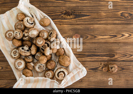 Fresche e pulite intero crudo baby bella funghi steso su un panno per asciugare su una tavola in legno rustico con pattern di grana di legno e spazio di copia Foto Stock