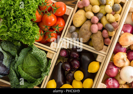Vista aerea su più gabbie di legno contenenti verdure comprese patate e cipolle su sfondo di legno Foto Stock