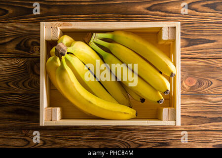 Scatola di legno con grappoli di fresche banane mature o dolce banane da cuocere su una tavola in legno rustico a un organico di mercato degli agricoltori visto vicino la parte superiore verso il basso Foto Stock