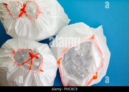 Tre bianchi sacchi riempiti con vuoto pulire le bottiglie di plastica pronti per essere raccolti per il riciclaggio e il riutilizzo su uno sfondo blu è vista dalla parte superiore verso il basso Foto Stock