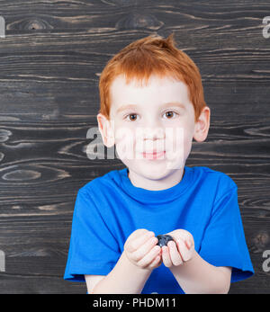 I capelli rossi boy tiene fuori un mirtillo bacche nelle mani aperte durante un pasto, close-up nella costruzione Foto Stock