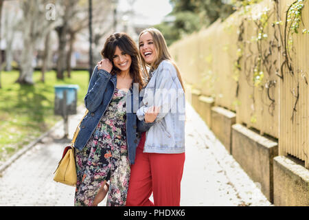 Due lieti di donne giovani amici abbracciando in strada. Bionda e bruna le ragazze che indossano un abbigliamento informale all'aperto. Foto Stock