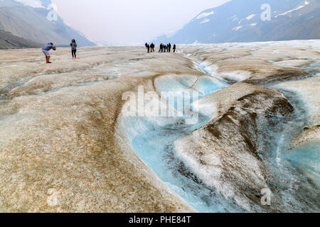 Superficie acqua allo stato fuso che fluisce attraverso il canale sinuoso sul Ghiacciaio Athabasca. Vi sono alcune persone in background ad esplorare il ghiacciaio a piedi Foto Stock