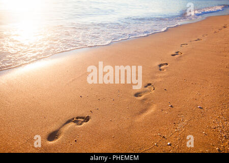 Spiaggia, onde e impronte in tempo al tramonto Foto Stock