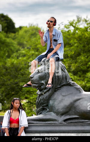 Giovane maschio caucasico si trova in cima a una statua di Lion e ascolta la musica con le cuffie a Mount Royal Park, Montreal, Canada Foto Stock