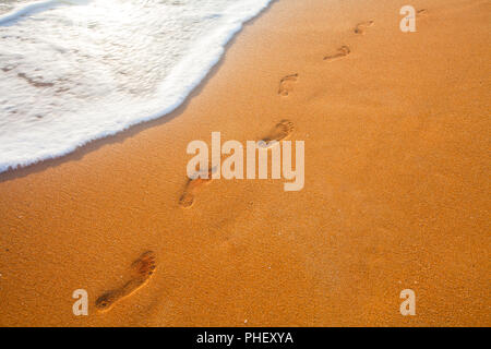 Spiaggia, onde e impronte in tempo al tramonto Foto Stock