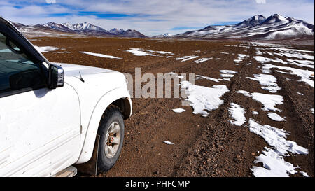 Un 4x4 veicolo spedizione passa attraverso il surreale paesaggio invernale e Snow capped paesaggio di montagna nel deserto SIloli, Sud Lipez provincia, Boliv Foto Stock