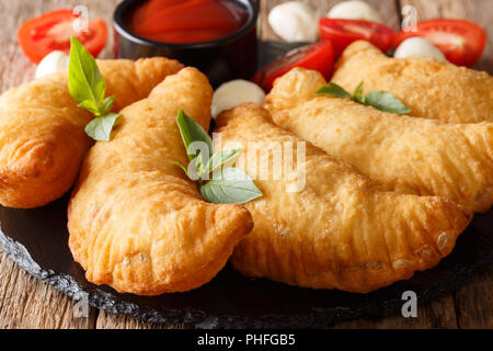 Italian fast food: panzerotti fritti con salsa di pomodoro, erbe aromatiche e mozzarella close-up su una lavagna nera. orizzontale, rustico Foto Stock