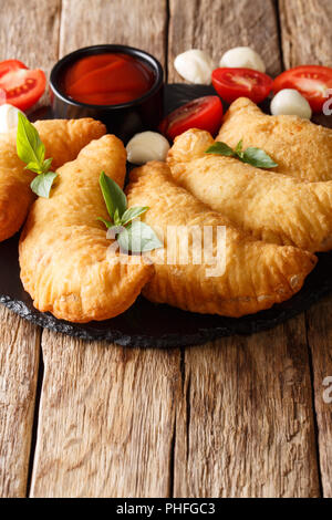 Delizioso caldo panzerotti fritti con salsa di pomodoro e mozzarella closeup su una tavola di legno verticale. Foto Stock