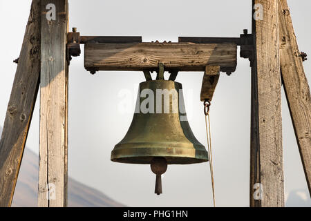 Una grande campana di bronzo appesa da una struttura in legno all'esterno. Foto Stock