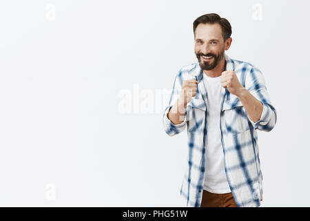 Vieni su attacco. Ritratto di bello gentile e giocoso uomo europeo con la barba, in piedi in posa boxer e tenendo sollevato i pugni mentre l'insegnamento figlio come lotta, sorridente ampiamente con la fotocamera Foto Stock