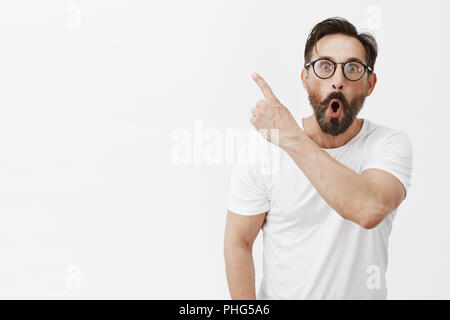 Fantastico look. Ritratto di sorpreso e impressionato bello uomo adulto con la barba e le rughe in bicchieri, puntando in alto a sinistra, facendo cadere la ganascia e la condivisione di impressioni con un amico Foto Stock