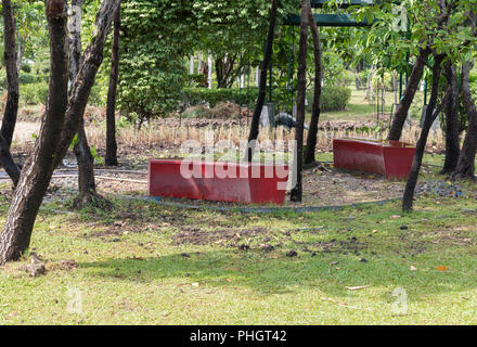 Rosso banco di plastica sono stati abbandonati nella zona del giardino del parco urbano. Foto Stock