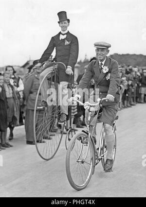 Penny Farthing bicicletta. Un uomo è a cavallo di un penny farthing bicicletta oltre ad un uomo su una normale bicicletta. 1930s Foto Stock