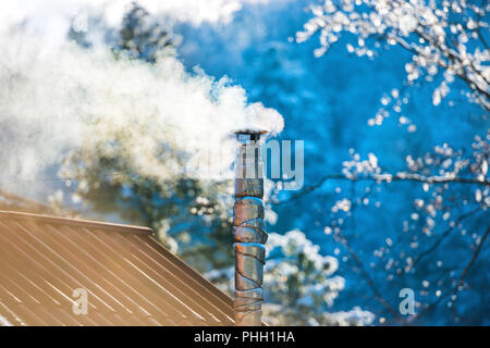 Il fumo dal camino sul tetto Foto Stock