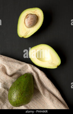 Intero e dimezzato avocadi sulla tavola nera, vista dall'alto. Foto Stock