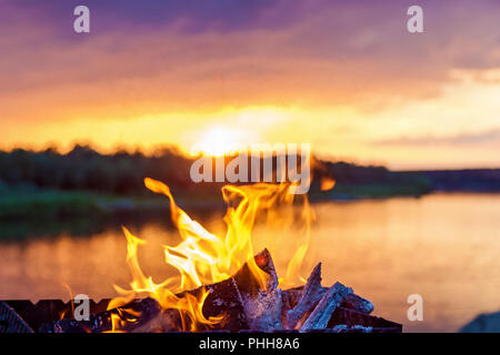 Red lingue di fiamma dal fuoco nei pressi del fiume al tramonto. Foto Stock